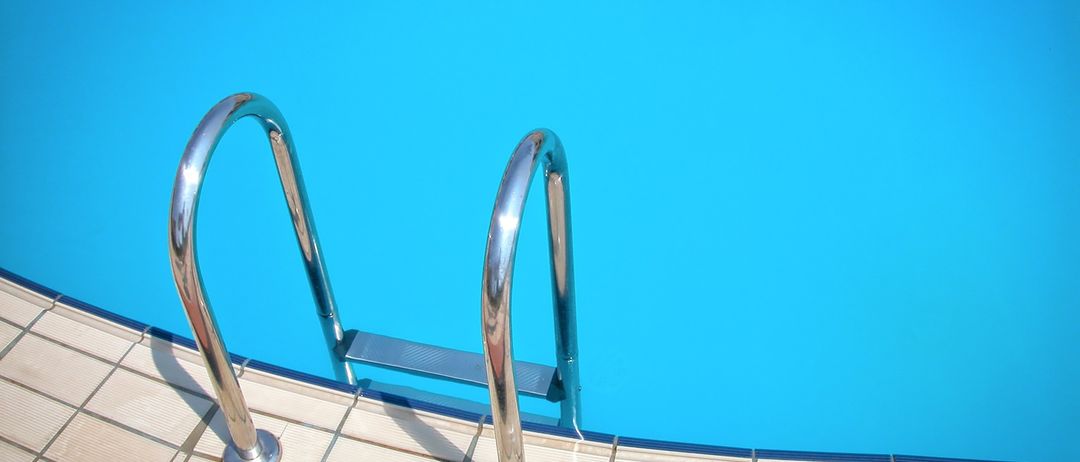 Ein leerer Swimmingpool mit einem Metallgeländer und einer gefliesten Kante. Das Wasser ist sauber und blau.