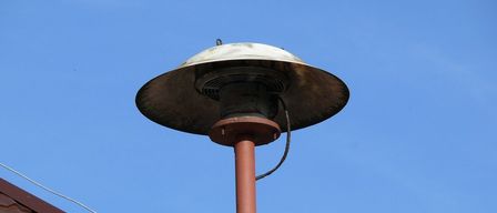 An outdoor heater with a red metal chimney is installed on a roof against a clear blue sky.