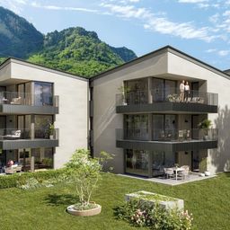 Ein modernes Apartmentgebäude mit Balkonen und Grünflächen, umgeben von üppigen Gärten und einer malerischen Bergaussicht.