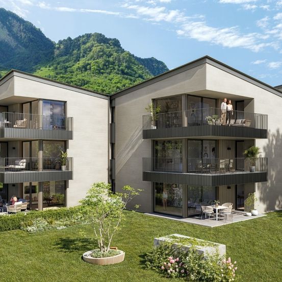 Ein modernes Apartmentgebäude mit Balkonen und Grünflächen, umgeben von üppigen Gärten und einer malerischen Bergaussicht.