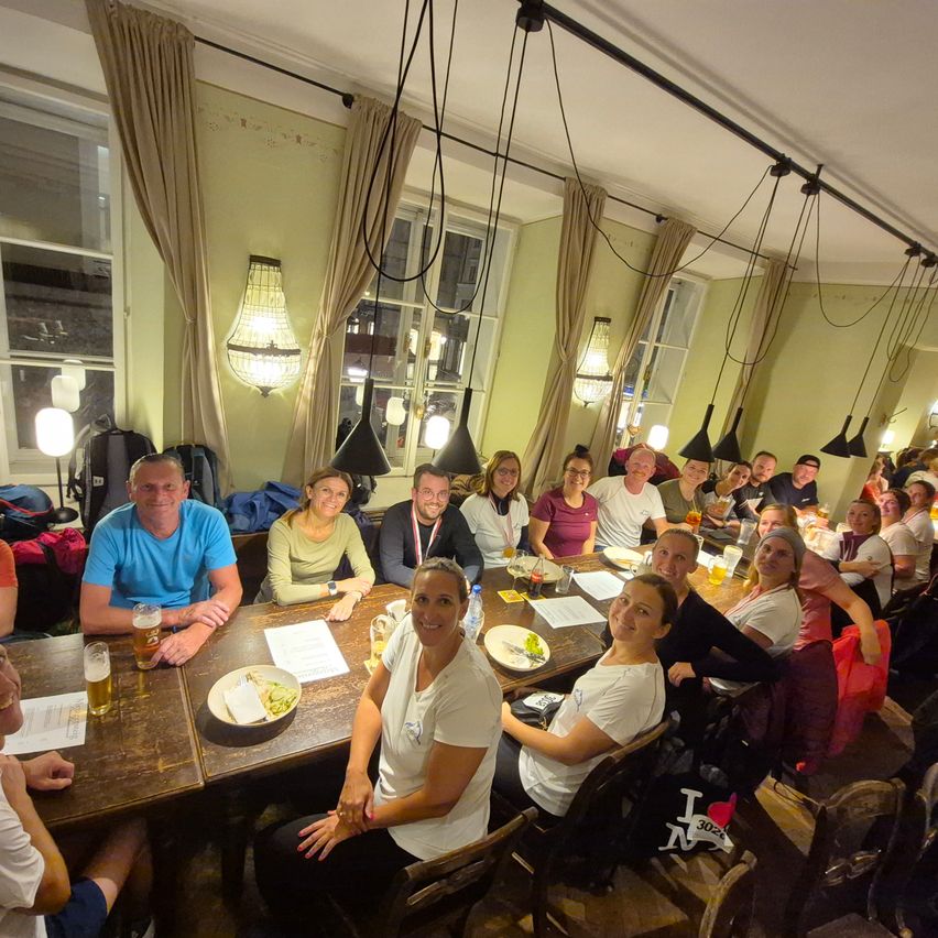 Eine Gruppe von Menschen sitzt an einem Tisch mit Tellern, Bechern und Papieren. Einige Leute lächeln und posieren für ein Foto.