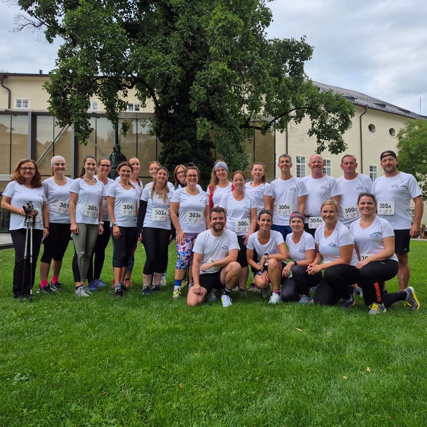Eine Gruppe von Menschen in weißen T-Shirts mit Nummern posiert für ein Foto auf einem Rasen vor einem Gebäude.