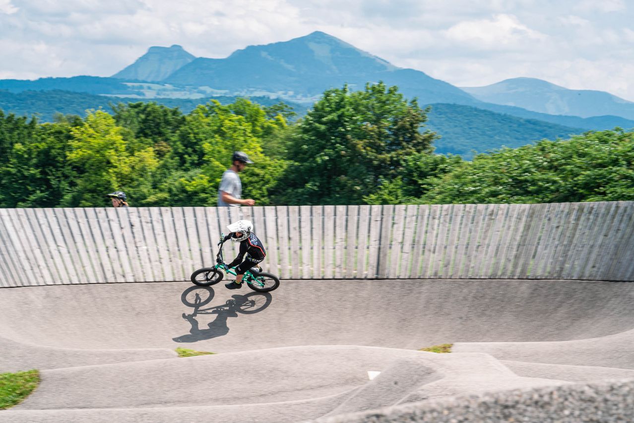 Ein junger Radfahrer fährt auf einer Strecke, umgeben von einem Holzzaun, mit Bergen im Hintergrund.