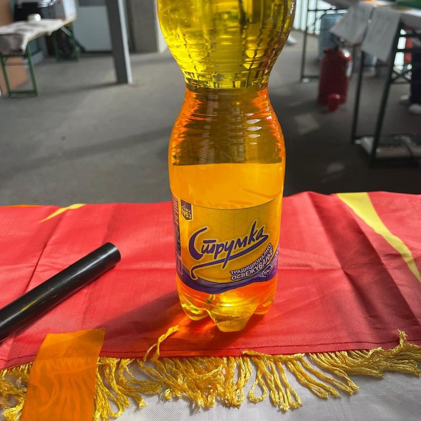 Eine Flasche Cupymak, ein traditionelles ukrainisches Getränk, steht auf einem Tisch, der mit einem rot-gelben Tuch und Quasten geschmückt ist. Ein schwarzes Objekt liegt in der Nähe.