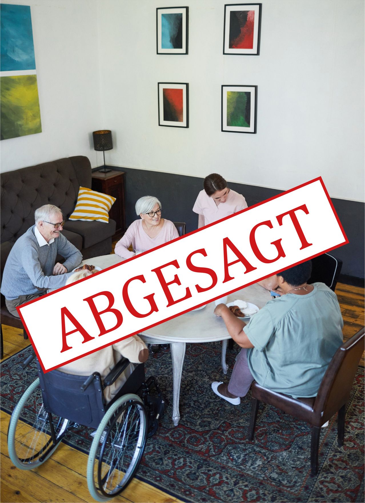 Eine Gruppe von Menschen, einschließlich älterer Personen und einer Frau im Rollstuhl, versammelt sich um einen Tisch. Eine Person lächelt, während eine andere in die Kamera schaut. Das Wort 'Abgesagt' ist prominent in Rot angezeigt.