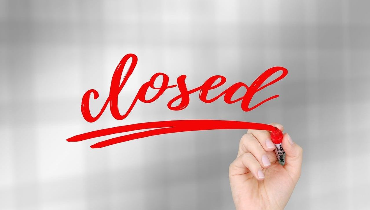 A hand holding a red marker writes 'closed' on a gray background. The marker is Pilot brand.