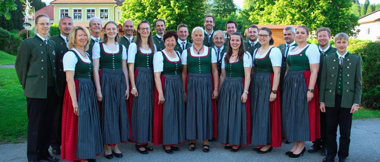 Eine Gruppe Erwachsener in traditioneller Kleidung posiert für ein Foto vor einem Gebäude mit Bäumen im Hintergrund.