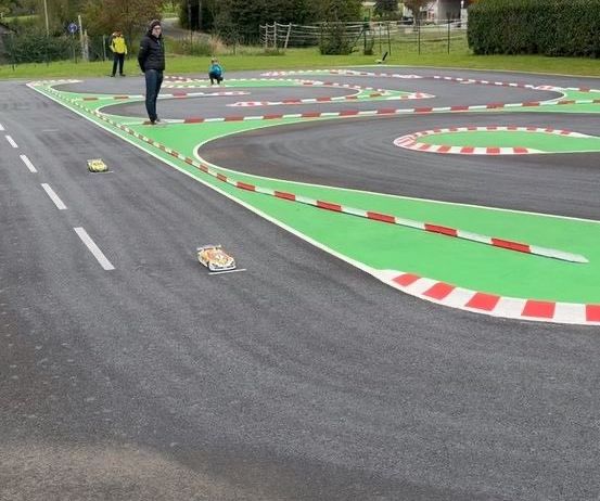Eine Outdoor-Rennstrecke mit grüner und roter Strecke und mehreren Leuten, die herumstehen. Es gibt zwei kleine Autos auf der Strecke.