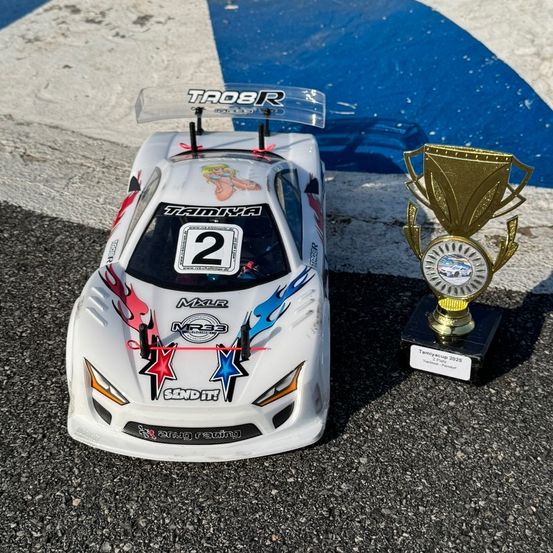 Ein weißer Rennwagen mit der Nummer 2 vorne und an der Seite steht neben einem Pokal auf einer Rennstrecke.