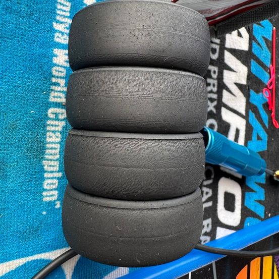 Vier schwarze Reifen, die aufeinandergestapelt sind, mit einem blauen Werkzeug verbunden, auf einem blau-weißen Hintergrund.