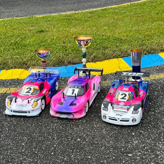 Drei Miniatur-Rennwagen mit den Nummern 1, 2 und 3 stehen auf einer Rennstrecke mit Siegerpokalen obenauf.