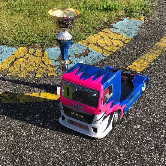 Ein blauer und pinker Rennwagen steht auf einer Straße neben einem Pokal. Der Wagen hat die Nummer 1 an der Seite.