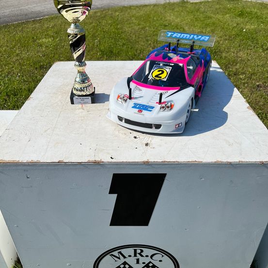 Ein weißer Podest mit der Nummer 1 darauf hält einen Pokal und ein Tamiya Rennwagen. Der Pokal trägt die Aufschrift TEC We Mountain 2019 und das Auto hat die Nummer 2.