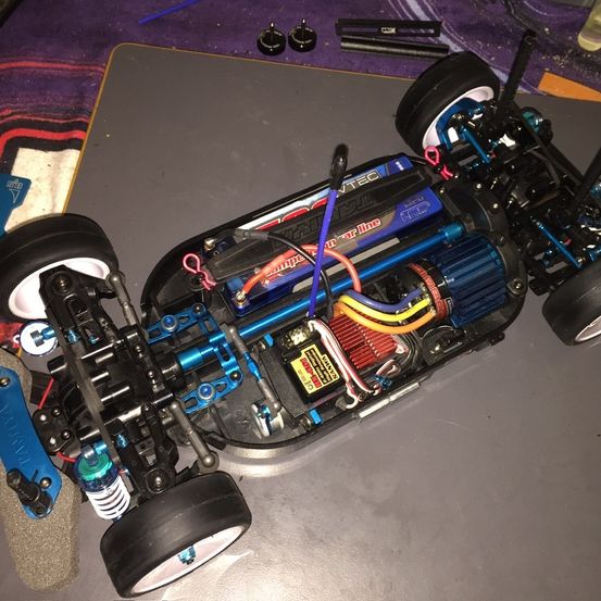 Nahaufnahme eines blauen und schwarzen ferngesteuerten Autochassis mit freiliegenden Kabeln und mechanischen Teilen.