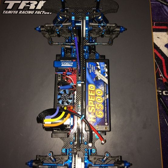 Eine Draufsicht auf ein Tamiya Racing Factory Modellauto mit blauen und schwarzen Komponenten, beschriftet mit 'HS-SPEED 6500', zeigt seine komplexen mechanischen Teile und Verkabelung.