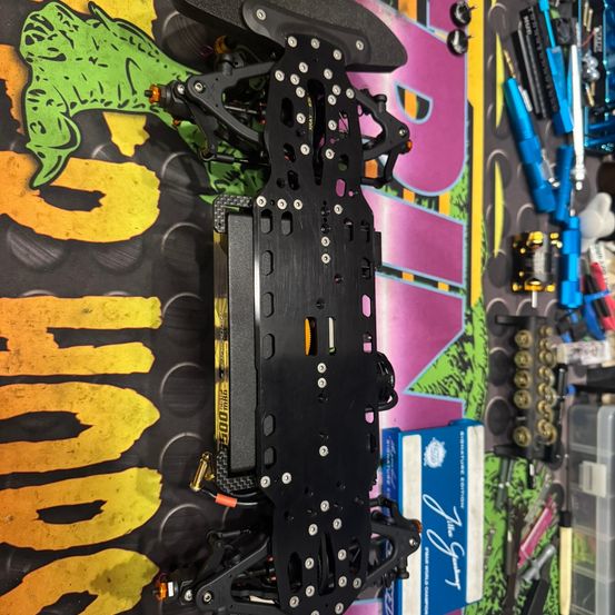 Eine Nahaufnahme eines schwarzen elektronischen Geräts, das auf einem farbenfrohen Hintergrund montiert ist, mit verschiedenen Werkzeugen und Teilen darum verstreut. Das Gerät hat eine rechteckige Form mit zahlreichen Schrauben und einem gelben Etikett mit der Aufschrift '500mAh'.