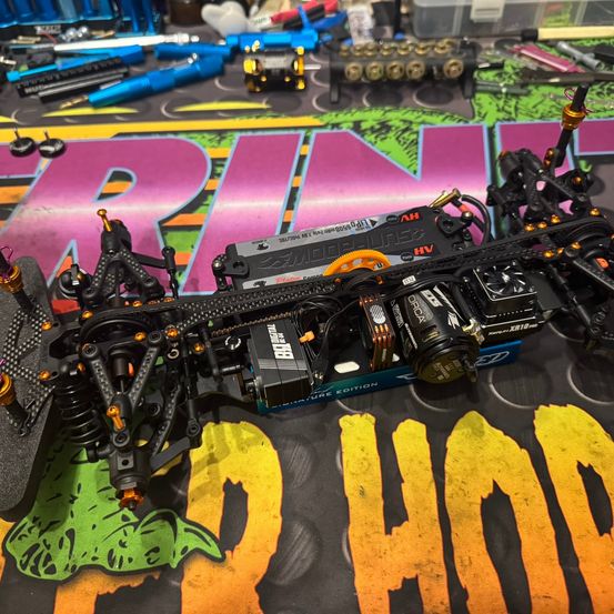 Ein RC-Auto wird auf einem bunten Hintergrund zerlegt. Verschiedene Werkzeuge und Teile sind darum verstreut.