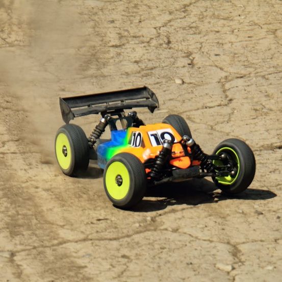 Ein ferngesteuertes Offroad-Auto mit der Nummer 10 auf der Vorderseite, das auf einem staubigen Pfad fährt. Das Auto hat einen farbenfrohen Körper mit grünen, blauen und gelben Reifen.
