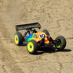 Ein ferngesteuertes Offroad-Auto mit der Nummer 10 auf der Vorderseite, das auf einem staubigen Pfad fährt. Das Auto hat einen farbenfrohen Körper mit grünen, blauen und gelben Reifen.