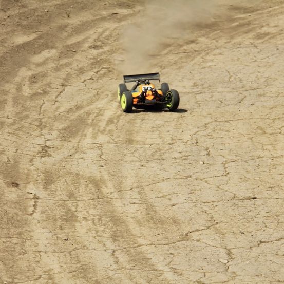 Ein orangefarbener und schwarzer Rennwagen mit der Nummer 10 fährt auf einer staubigen Erdstrecke. Der Wagen wirbelt Staub auf, während er sich bewegt.