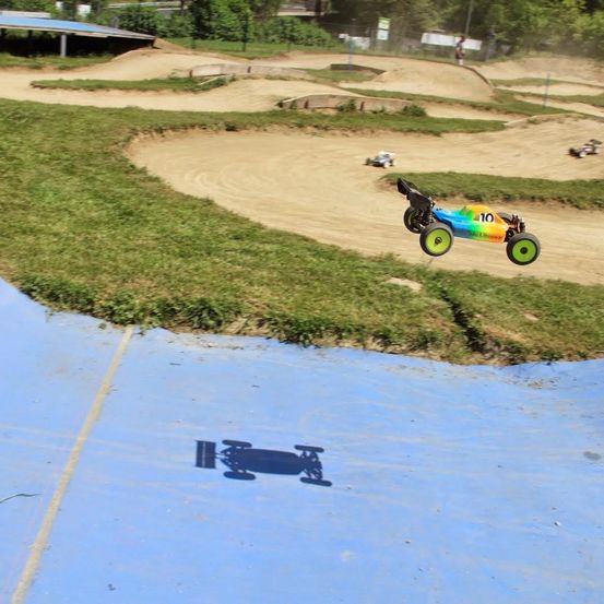 Ein ferngesteuertes Auto auf einer Dirt-Rennstrecke mit Gras an den Seiten. Andere Autos sind in der Ferne. Das Auto hat die Nummer 10.
