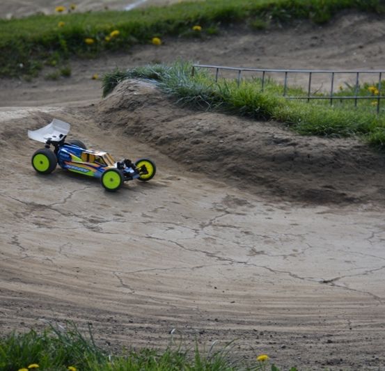 Ein blaues und gelbes ferngesteuertes Auto fährt auf einer schlammigen Strecke mit Reifenspuren und einer kleinen Rampe an der Seite.