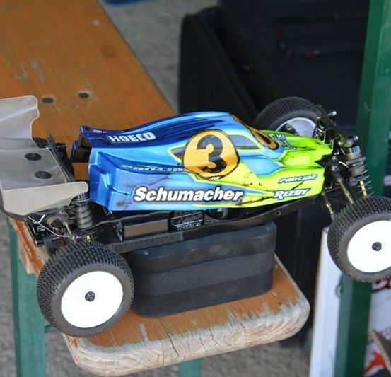 Ein blauer und grüner Schumacher Rennwagen mit der Nummer 3 ruht auf einer Holzbank.