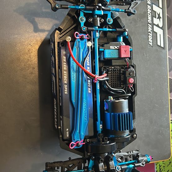 Das Bild zeigt die Rückseite eines blauen und schwarzen RC-Autos mit sichtbaren Komponenten, einschließlich Drähten, einem Akku und Teilen, die mit HYLG STOCK SPEC gekennzeichnet sind.
