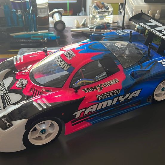 Ein Tamiya MR33 Rennwagen mit einem lebhaften roten und blauen Design steht auf einem Tisch mit verschiedenen Werkzeugen und Ausrüstung im Hintergrund.