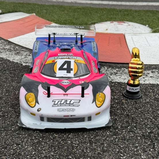 Ein ferngesteuertes Rennauto mit der Nummer 4 an der Front steht auf einer Rennstrecke neben einem Pokal.