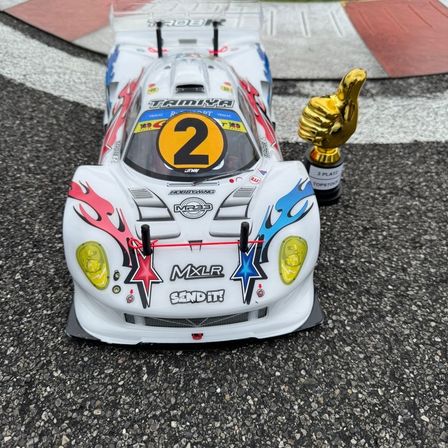 Ein weißer Rennwagen mit der Nummer 2 auf der Vorderseite und einem Pokal in der Nähe auf einer Rennstrecke.