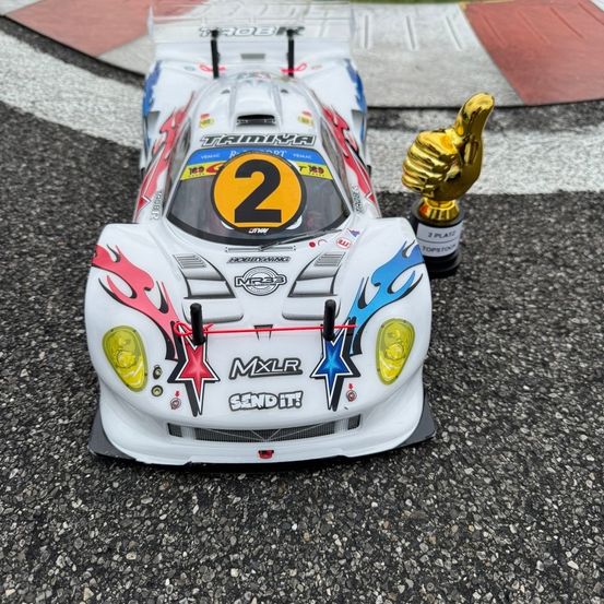 Ein weißer Rennwagen mit der Nummer 2 auf der Vorderseite und einem Pokal in der Nähe auf einer Rennstrecke.