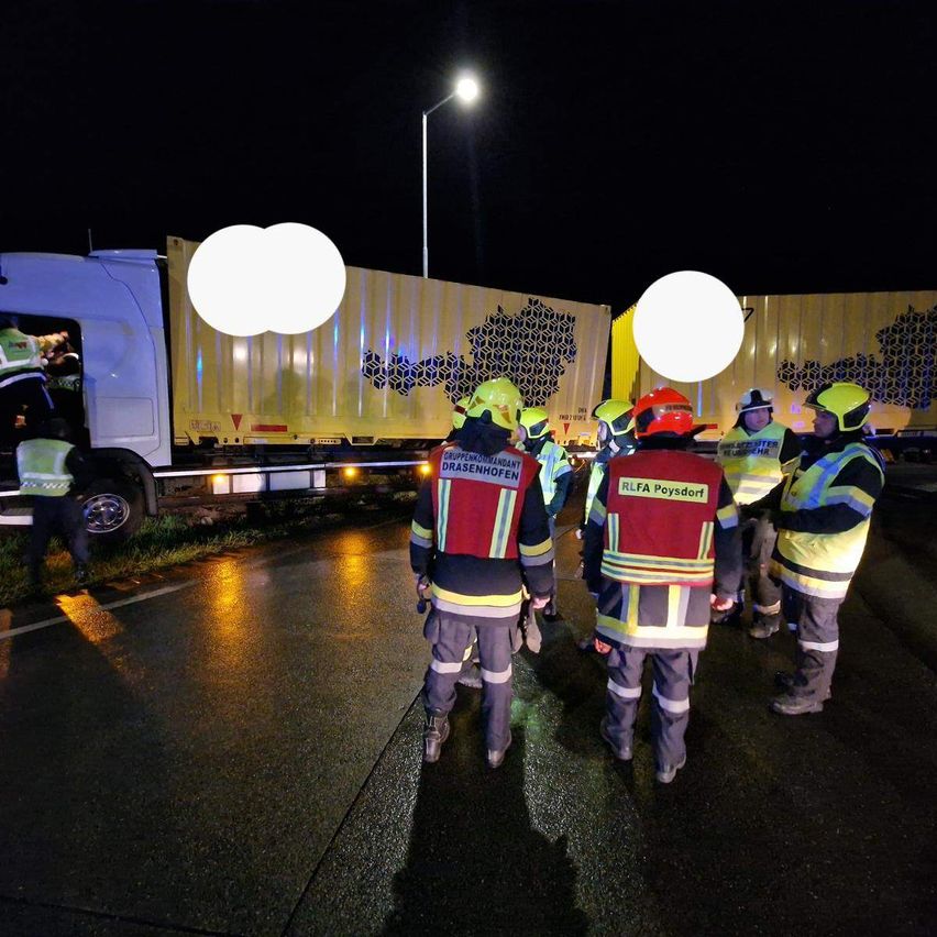 In der Nacht versammeln sich Rettungskräfte um einen gelben LKW mit Logo an der Seite, einer der Helfer trägt einen Helm mit dem Namen "RLFA Poysdorf".