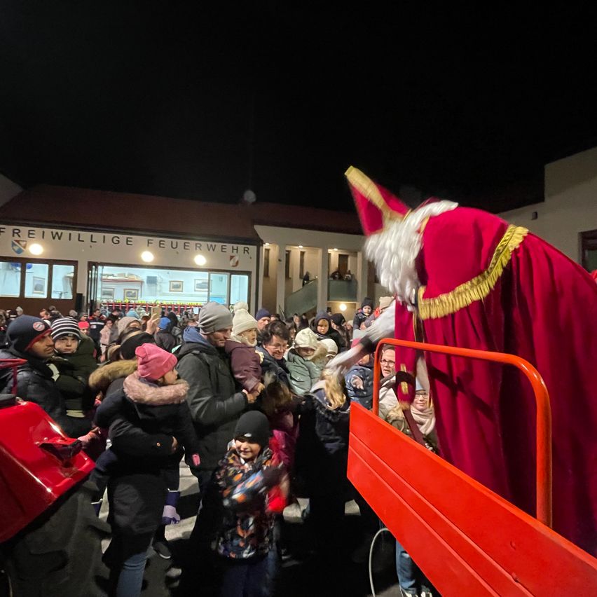 In der Nacht versammelt sich eine Menschenmenge um einen als Weihnachtsmann gekleideten Mann in einem roten Outfit, der auf einem roten Lastwagen vor einem Gebäude steht.
