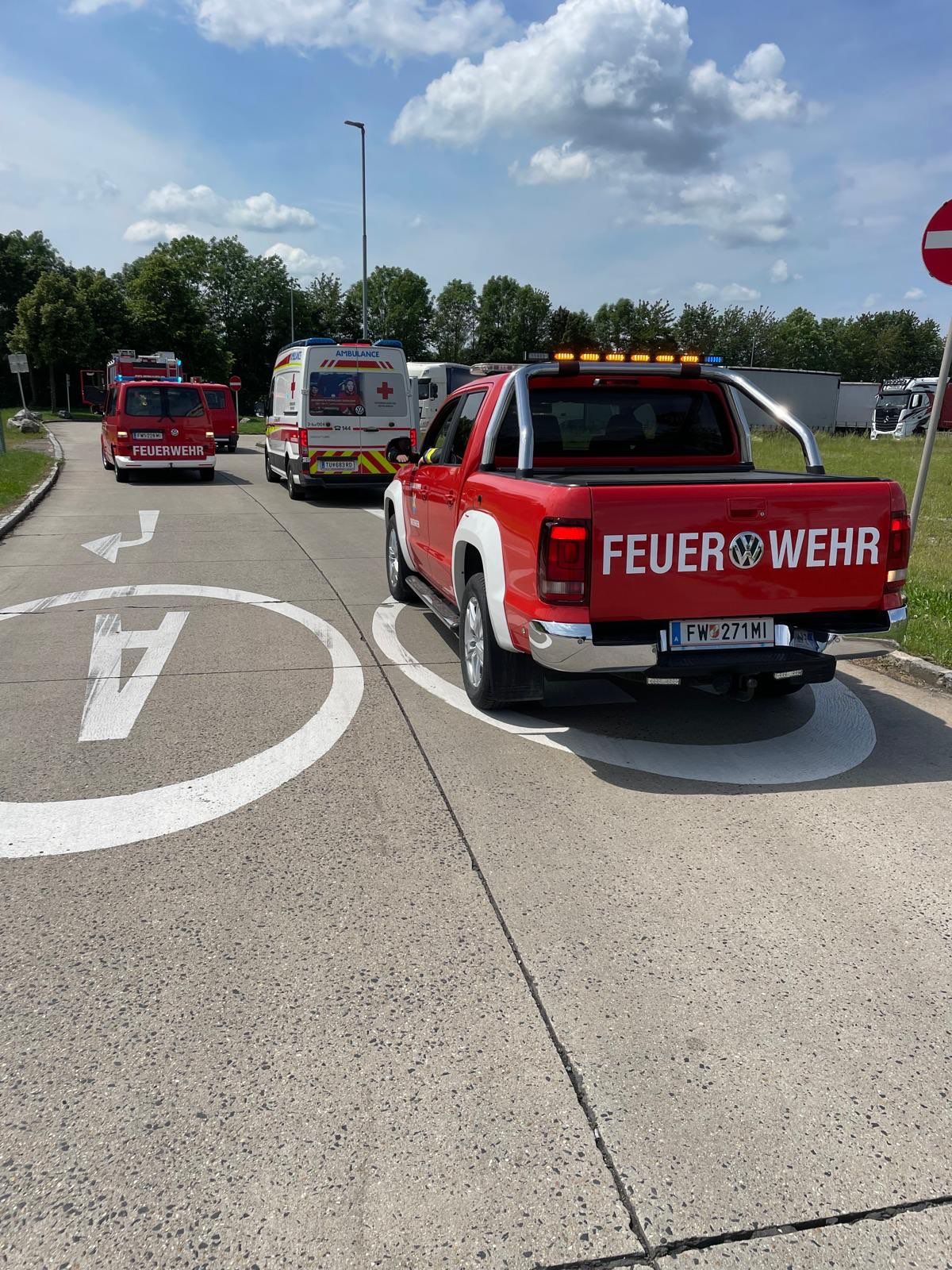 Ein roter Pickup-Truck mit 'FEUER WEHR' auf der Rückseite fährt auf der Straße mit Rettungsfahrzeugen. Er ist in einem ausgewiesenen Bereich geparkt.