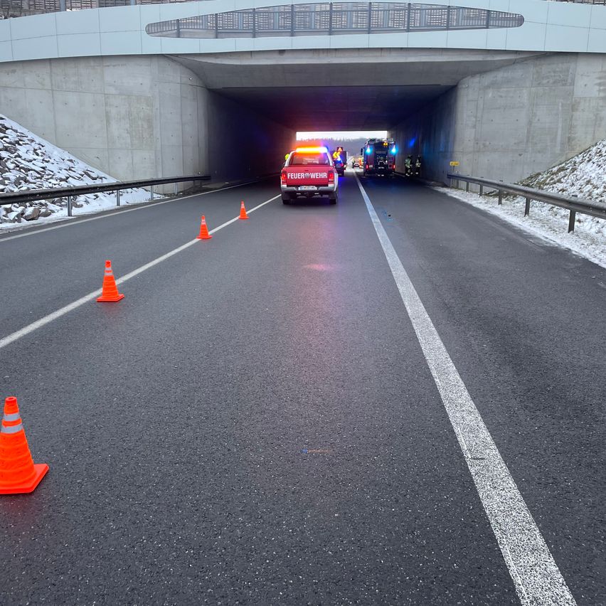 Eine Straße mit Einsatzfahrzeugen, einschließlich eines Feuerwehrwagens, ist teilweise durch Verkehrskegel blockiert. Die Straße führt in einen Tunnel.