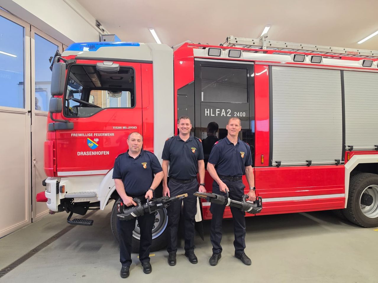 Drei Feuerwehrleute stehen vor einem Feuerwehrauto mit der Aufschrift HLFA2 2400 und halten Kettensägen. Sie tragen Uniformen mit Drasenhofen auf der linken Seite.