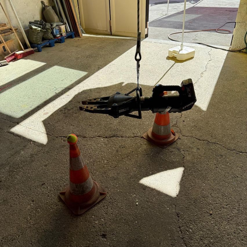 A black tool with the word Force on it is suspended in the air by ropes, next to two orange traffic cones in a garage.