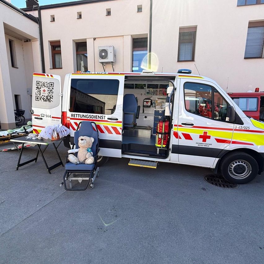 An ambulance with the number 144 is parked in front of a building. A teddy bear sits on a chair next to the open door.