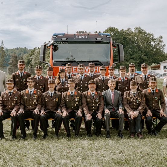 Eine Gruppe von Männern in Militäruniformen posiert für ein Foto vor einem orangefarbenen Lastwagen.