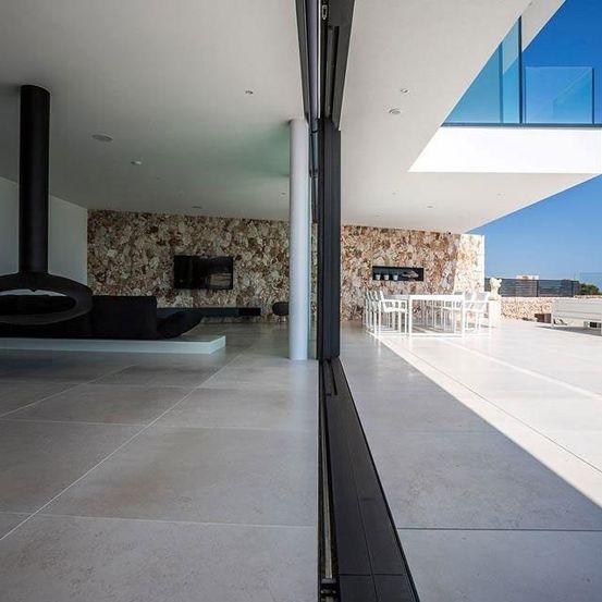 Ein modernes Haus mit großen Glasfenstern, einem Kamin und einem Essbereich mit weißen Stühlen und Tischen. Das Haus hat eine Steinwand und einen klaren blauen Himmel.