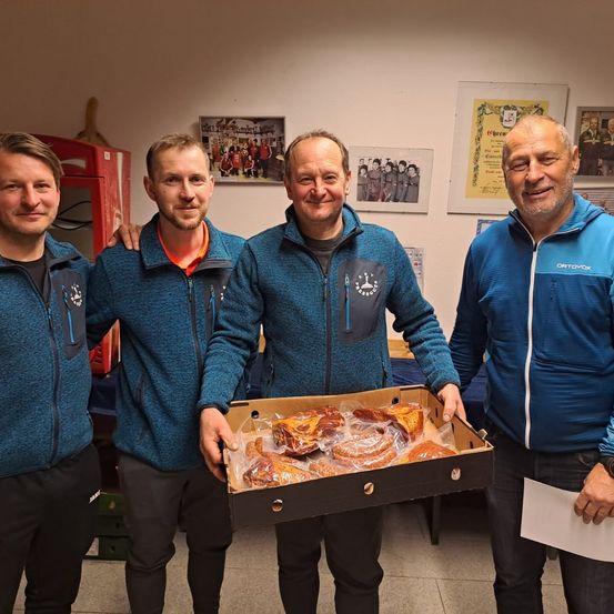 Vier Männer stehen nebeneinander, wobei einer eine Schachtel mit Gebäck hält.