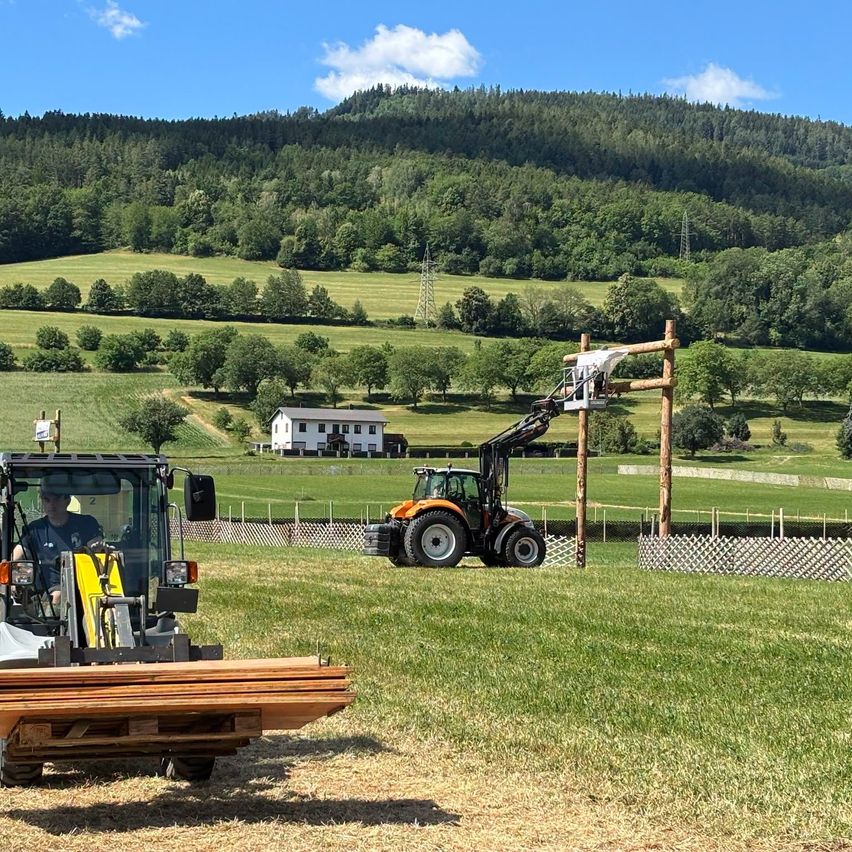 Traktor mit Kran hebt Mann an Holzbalken in Steiermark, Österreich