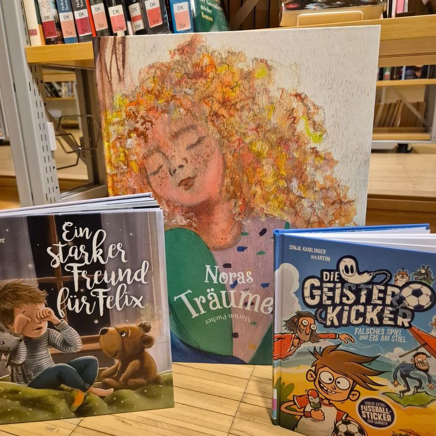 Books on a wooden table in front of a bookshelf with a painting of a girl asleep. The books include 'A Stronger Friend for Felix', 'Nora's Dreams', and 'The Ghost Kicker'.