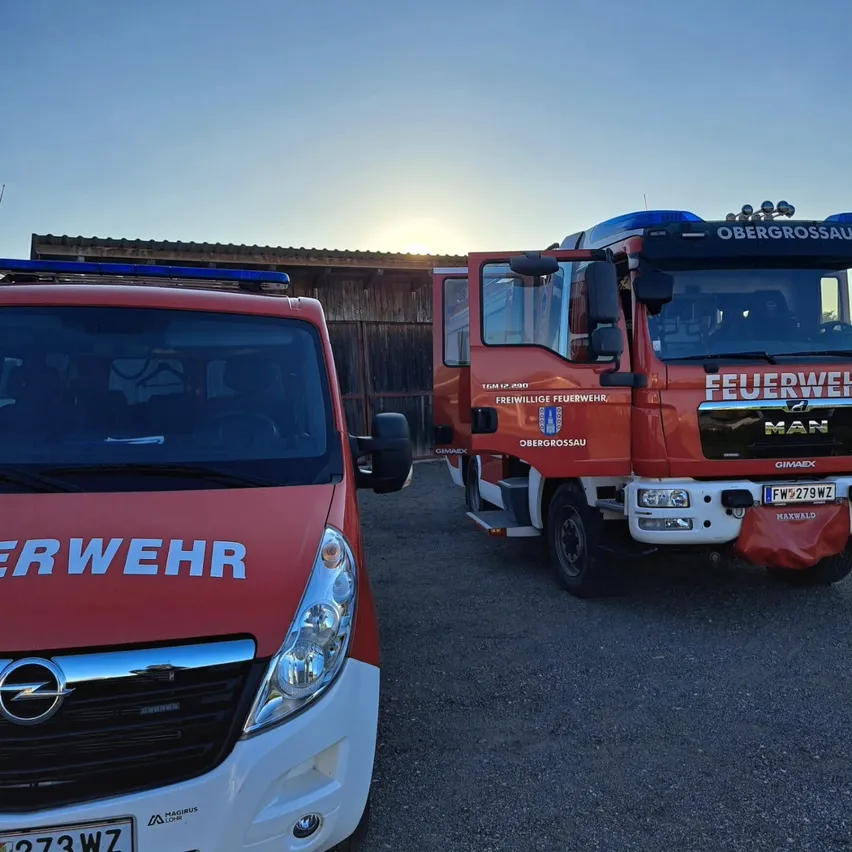 Zwei Feuerwehrfahrzeuge, eines rot und weiß und das andere rot mit blauem Dach, stehen am Straßenrand geparkt.
