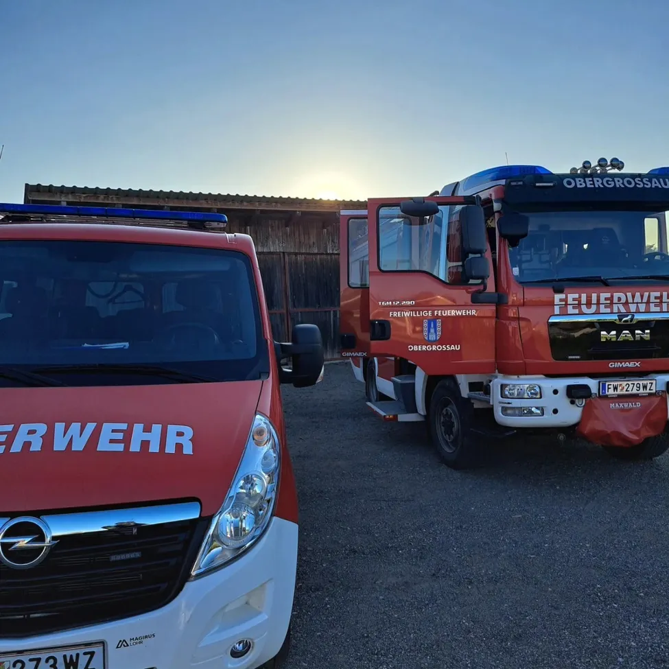 Zwei Feuerwehrfahrzeuge, eines rot und weiß und das andere rot mit blauem Dach, stehen am Straßenrand geparkt.