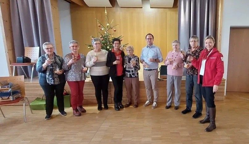 Eine Gruppe von Menschen steht zusammen in einem Raum und hält Weingläser. Ein Weihnachtsbaum steht hinter ihnen.