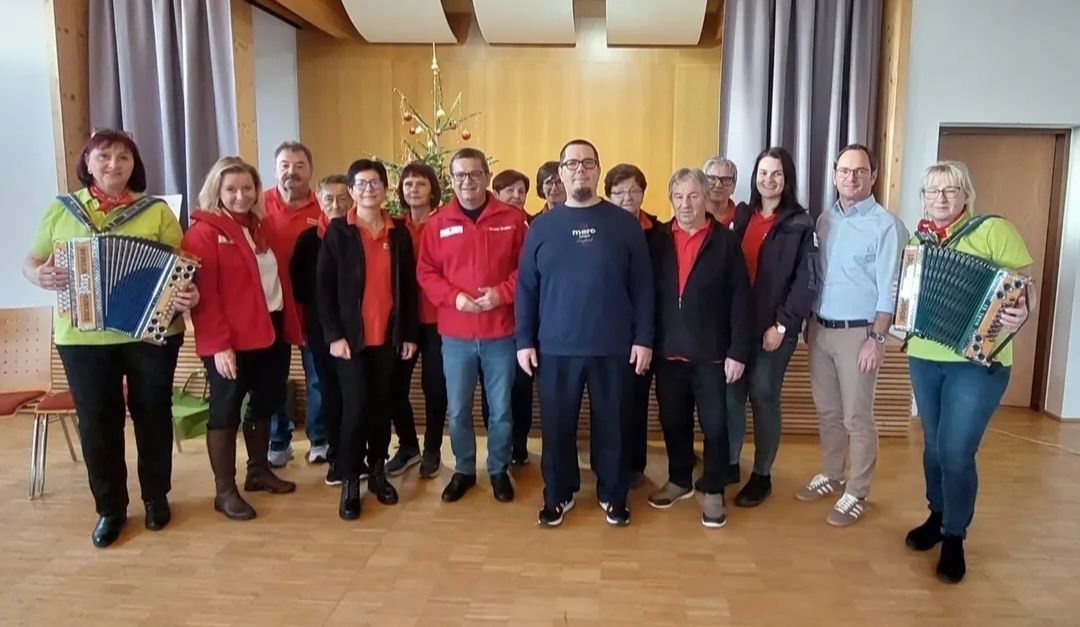 Eine Gruppe von Erwachsenen in roten und blauen Jacken, Brillen und Turnschuhen posiert für ein Foto auf einem Holzboden vor einem Weihnachtsbaum.