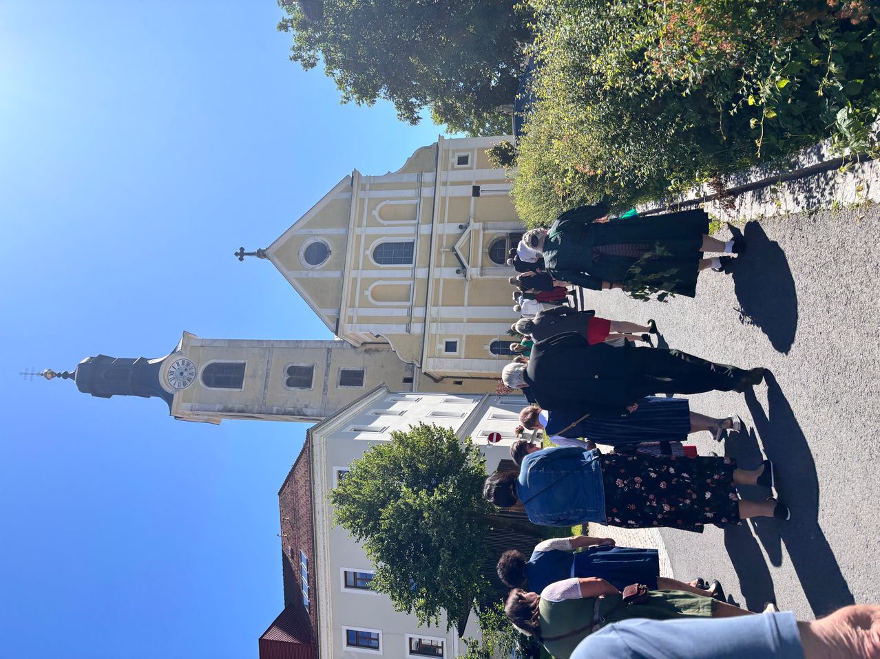 A group of people are gathered in front of a large church with a clock tower. They are dressed in traditional clothing.