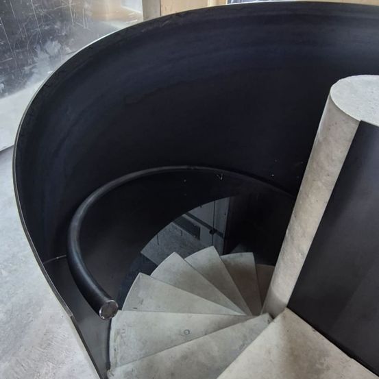 Eine moderne Wendeltreppe mit schwarzem Handlauf und Betonstufen. Die Treppe scheint aus Beton mit einer glatten Oberfläche zu sein.